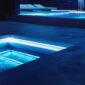 a sleek, modern outdoor pool area glistens under bright, artificial lighting, showcasing pristine blue water and vibrant pool equipment, emphasizing the importance of weekly maintenance for aesthetic appeal and cleanliness.
